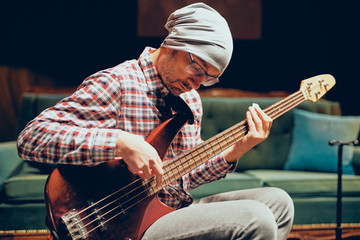 Obraz premium Young Caucasian man with hat on head playing acoustic guitar while sitting in home studio.