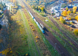 Aerial view on blue passenger train moving on rails in city area.