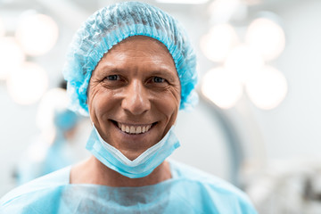 Emotional enthusiastic doctor feeling happy and smiling while standing alone with medical hat on his head