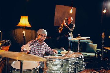 Two men playing drums and saxophone in home studio.
