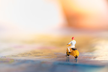 Travel Concept. Woman  traveler miniature figures ride motorcycle / scooter on world map.