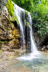 Obraz premium Waterfall Jur-Jur in summer, green moss and water, Crimea, Russia. White streams of water falling from a large stone in the forest, green moss around, green water