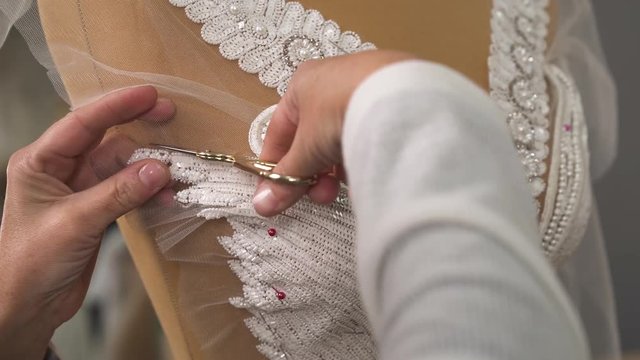 Female hands cutting off the veil cloth sequined and beaded lace fixed on the mannequin and adjusting it to model a better outcut