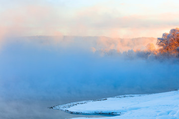Winter landscape of trees and river in a foggy morning. Frost and cold and sunshine.