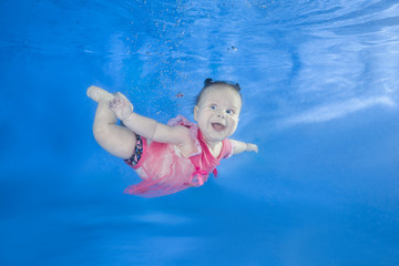 Little baby in pink dress swim underwater. Baby swimming underwater in the pool on a blue water...