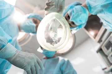 Bottom view of three professional doctors leaning over the patient and wearing medical masks while holding the anesthetic inhaler