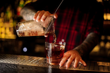 Fototapeta na wymiar Mixologist pouring fresh strong whiskey cocktail into a glass