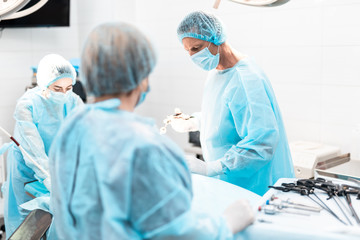 Portrait of focused doctor in protective mask performing surgery in modern operating room while...