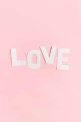 Word Love made of letters cut out of paper on a pink pastel background