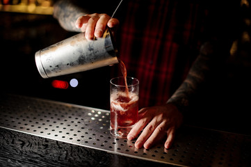 Fototapeta na wymiar Mixologist pouring sweet juicy cocktail into a glass on bar