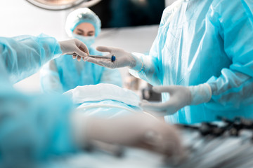 Laparoscopic instrument. Close up of female hands in sterile gloves giving trocar for laparoscopy procedure to doctor