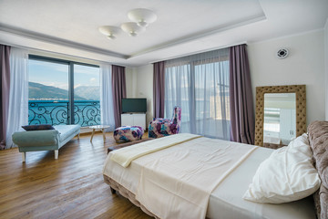 Fototapeta na wymiar Interior of a spacious light bedroom with sea view in a luxury villa. Big comfortable double bed in elegant modern bedroom