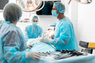 Side view portrait of focused doctor in sterile gloves holding laparoscopic instrument while...