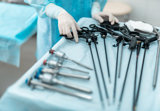 Close up of female hand holding laparoscopic scissors or grasper. Lady wearing blue surgical gown