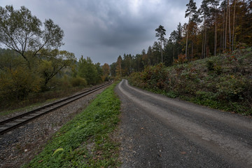 Fototapeta na wymiar forest path next to train tracks under storm clouds in autumn