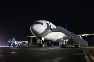 Naklejka na ściany i meble Wide-body passenger airplane with boarding stairs at the night airport apron. Aircraft ground handling