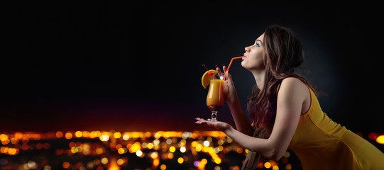 Fototapeta premium Young beautiful girl with cocktail on a background of night city.