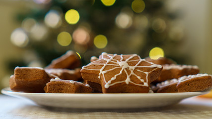 Selective focus on gingerbread cookies on a plate on a Christmas blurred background with decorated tree and glittery fairy lights. Winter Holiday concept.