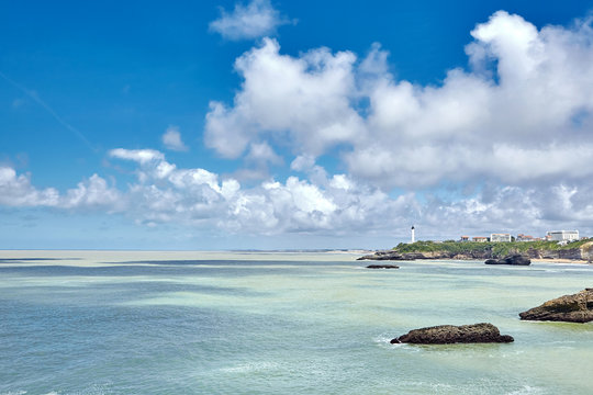 Seascape. Biarritz city, ocean water and a lighthouse on the skyline. Bay of Biscay, Atlantic coast, Basque country, France. Summer sunny day and blue sky with white clouds