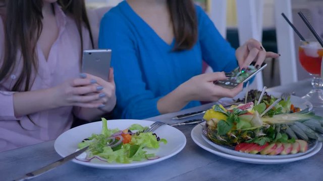 hands of women friends using mobile phone for photo of beautiful salad during healthy dinner during diet for weight loss in restaurant close-up