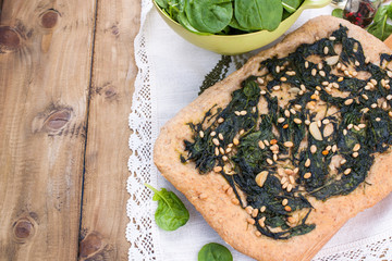 Traditional pie with spinach and nuts. Tasty homemade pastry on wooden background. Photo in the style of rustic. Fresh green vegetables. Italian food. Free space to copy text.