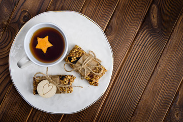 Homemade granola oatmeal energy bars, and cup of tea wyth orange star on white plate, healthy snack, copy space on wood desk