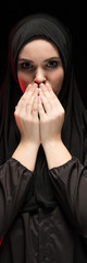 Portrait of beautiful serious young muslim woman wearing black hijab with hands near her face as praying concept on black background