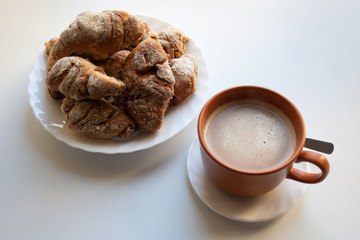 Heap of crusty croissants and cup of warm coffee isolated on white background