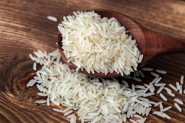 White jasmine rice in wooden spoon on dark table background