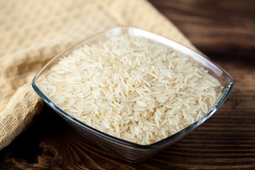 Seeds of white rice in glass bowl on wooden table, ingredient for cooking