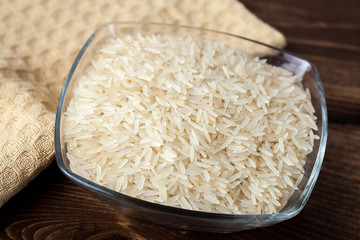 Seeds of white rice in glass bowl on wooden table, ingredient for cooking