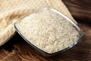 Seeds of white rice in glass bowl on wooden table, ingredient for cooking