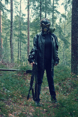 woman in black with a gas mask on her head and an automatic rifle wanders viciously through the forest in search of innocent victims thirsting for blood
