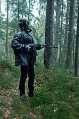 woman in black with a gas mask on her head and an automatic rifle wanders viciously through the forest in search of innocent victims thirsting for blood