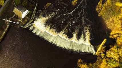 Aerial image looking directly down on the dark waters of a river flowing over a weir, and a fish ladder.