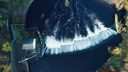 Aerial image looking directly down on the dark waters of a river flowing over a weir, and a fish ladder.
