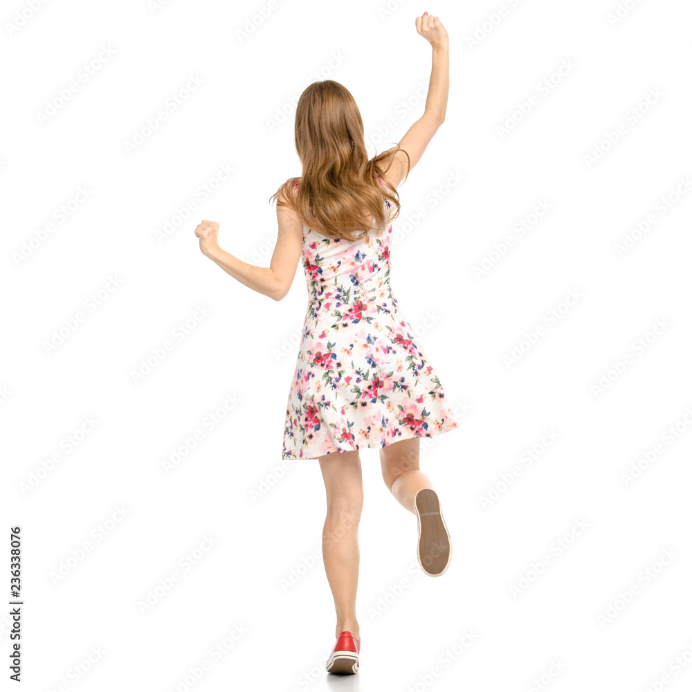 Wall mural beautiful woman in dress with flowers print and sneakers showing of positive emotions runs happy bac