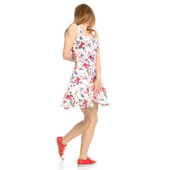Beautiful woman in dress with flowers print and sneakers showing of positive emotions goes happy back view on white background isolation