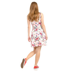 Beautiful woman in dress with flowers print and sneakers showing of positive emotions goes happy back view on white background isolation
