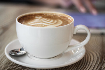 cup of coffee on a wooden table on a background of young woman works with digital tablet