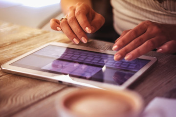 young woman works with digital tablet on a background of cup of coffee on a wooden table