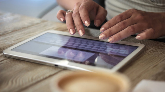 young woman works with digital tablet on a background of cup of coffee on a wooden table