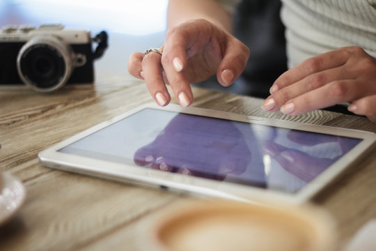young woman works with digital tablet on a background of cup of coffee on a wooden table