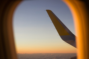 Window of airplane and the views of the yellow and white wing blue sunset sky. Business trip, summer holidays, travel concepts