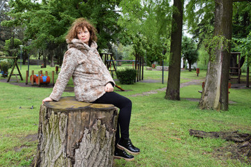Portrait of a beautiful woman resting in the park on a stump in the afternoon