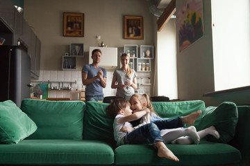 Happy funny preschool cute girl hug boy, sister and brother playing together on sofa at home,...