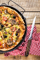 pizza with cheese, tomatoes, mushrooms, ham, sausage and olives on a wooden table, top view