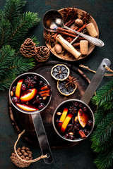 hot mulled wine cooked in two saucepan with spices, orange and cranberries on the table with Christmas fir twigs on a dark background