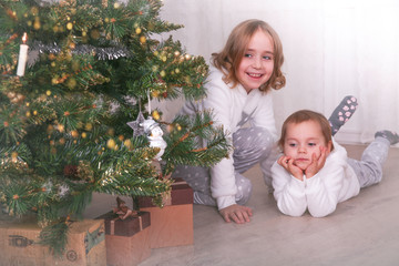 Two adorable little sisters looking for gifts under a Christmas tree on Christmas eve at home. Snowflakes texture