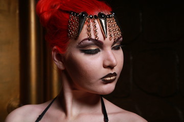 beautiful girl with red hair in an Egyptian style with gold jewelry and Cleopatra makeup standing...